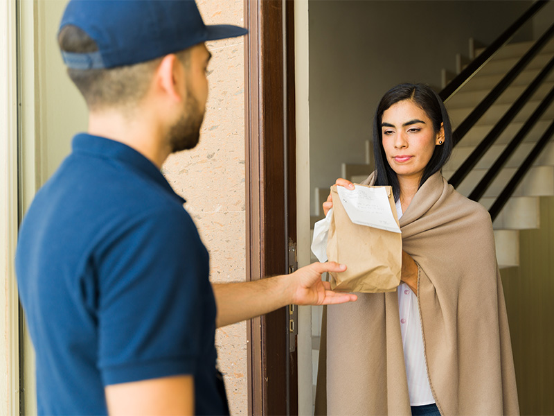 Medikamente nach Hause liefern: Kurier übergibt einer Frau Medikamente, Fläschchen und Kapseln sicher verpackt.