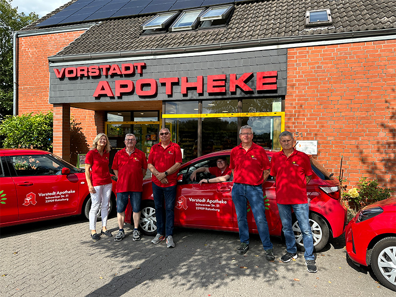 Arzneimittellieferservice in Ratzeburg: Vorstadt-Apotheke Botenteam vor roten Lieferautos bereit für Hauslieferungen.