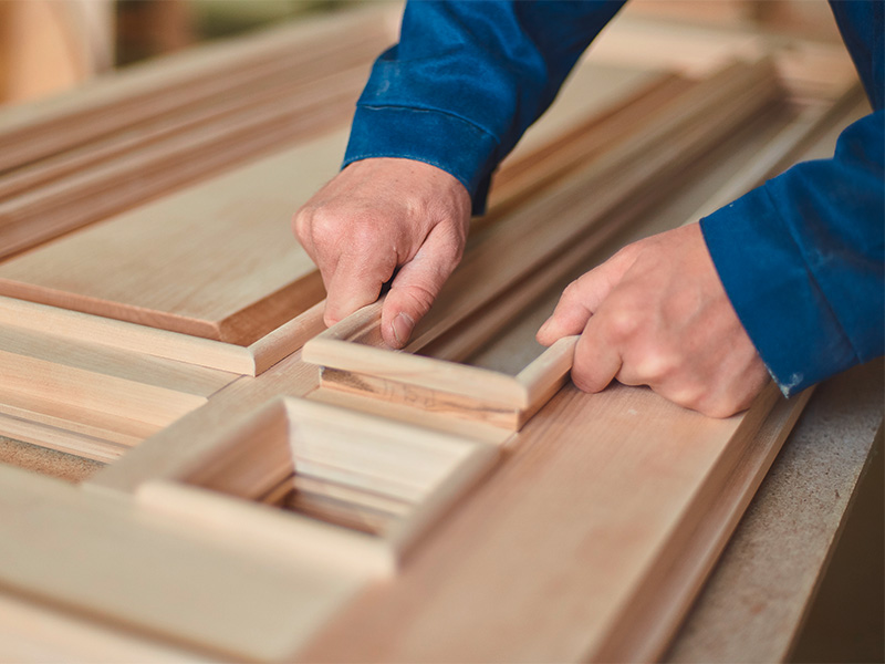 Bautischler bearbeitet ein Holzbauteil in der Werkstatt und führt präzise Arbeiten mit professionellen Werkzeugen aus.