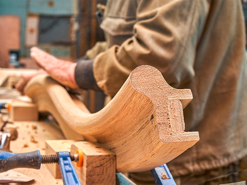 Erfahrener Tischler schleift ein gebogenes Holzgeländer sorgfältig von Hand für eine hochwertige Treppenkonstruktion.
