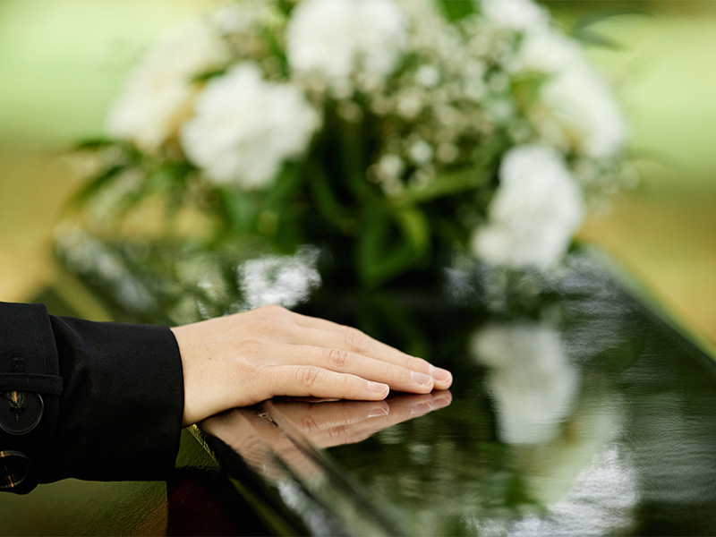 Trauernde Hand auf Sarg während Zeremonie im Freien, Symbol für würdevolle Erdbestattung in Ratzeburg und Abschied.