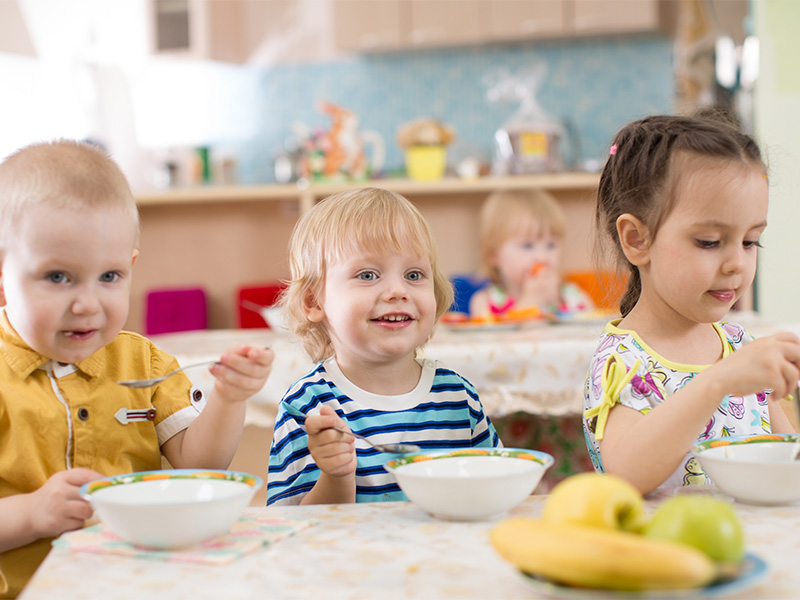 Kinder im Kindergarten essen gemeinsam gesundes Essen an Tisch, abwechslungsreiche Mahlzeiten und fröhliche Verpflegungssituation beim Mittagessen.